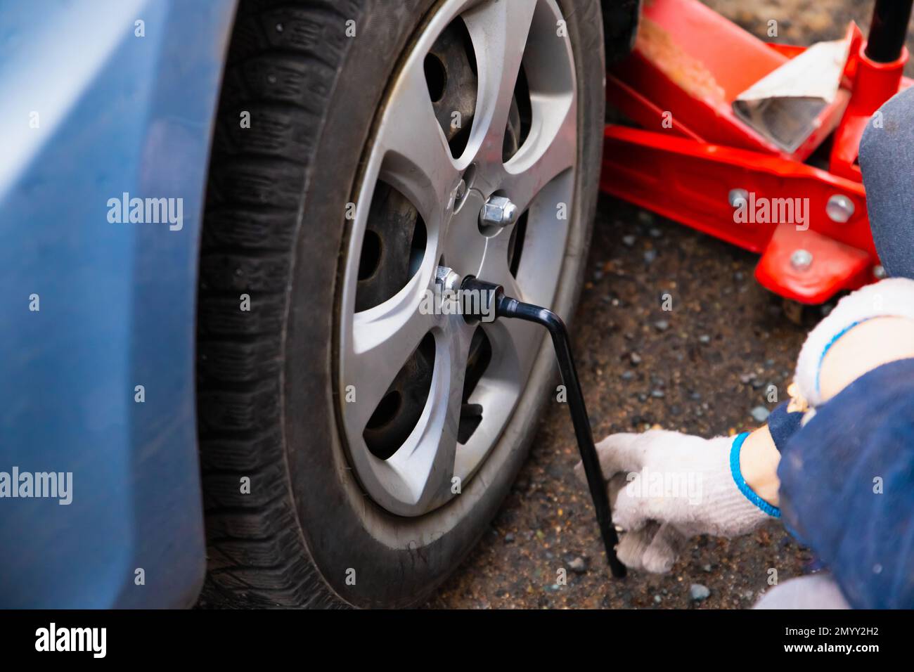 Changement de roue, la voiture est soulevée à l'aide d'un cric. Les mains mâles dévisse les rondelles de roue à l'aide d'une clé à bille. Banque D'Images