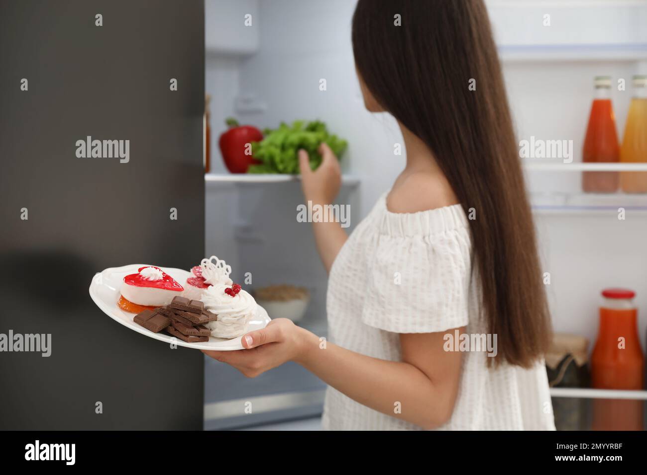 Concept de choix entre la nourriture saine et la malbouffe. Femme tenant une assiette avec des bonbons près du réfrigérateur dans la cuisine, se concentrer sur la main Banque D'Images