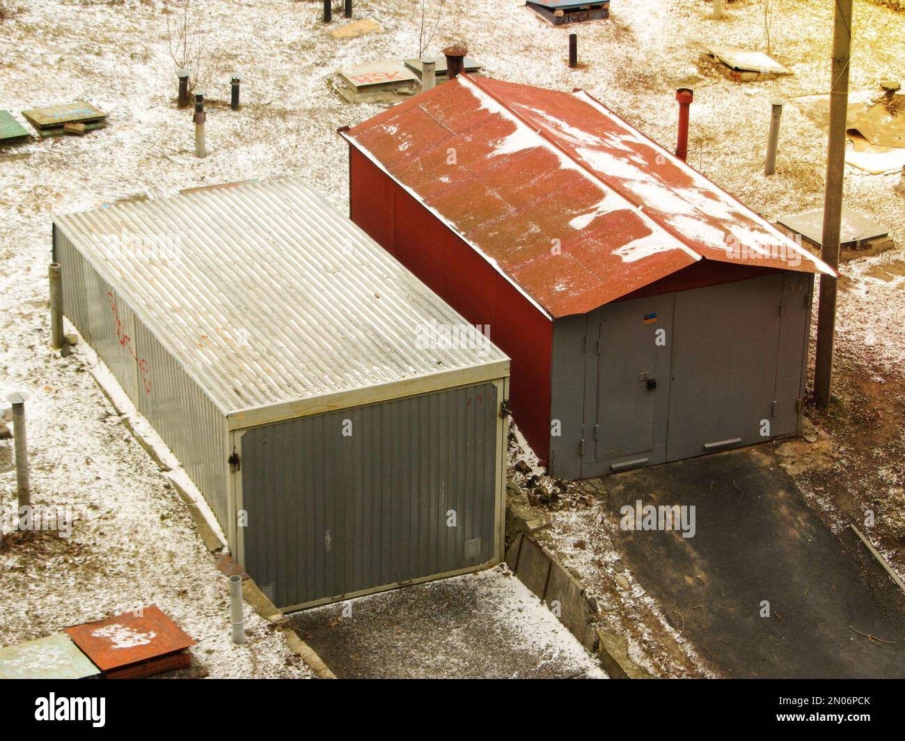 Deux vieux garages de voitures en métal comme vu d'en haut en hiver. Un vieux garage en métal rouge gris sur un mur de clôture dans une rue rurale. Ancienne porte métallique Banque D'Images