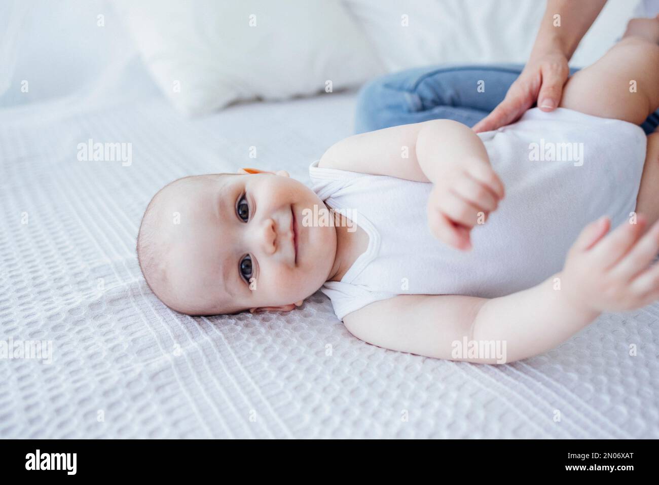 Jeune belle mère embrassant son bébé mignon sur la joue. La brune blanche touche son enfant souriant avec son visage. Joli bébé dans un body blanc avec Banque D'Images