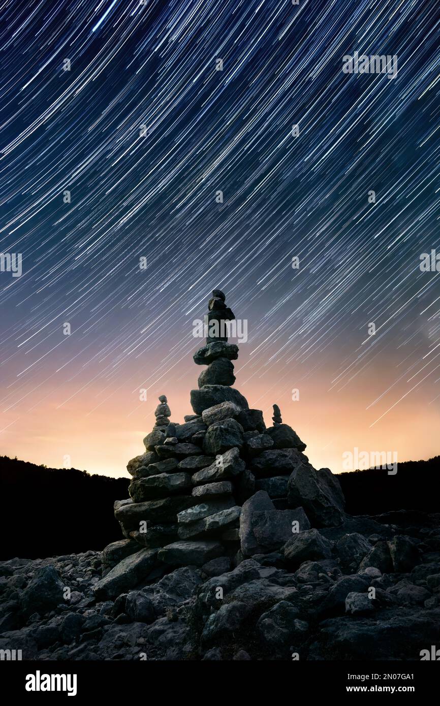 Ciel nocturne avec pistes étoiles sur arrangement de pierre équilibrée empilée, composition verticale centrée Banque D'Images