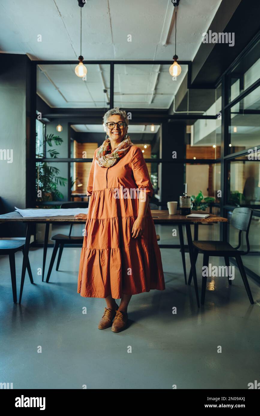 Femme d'affaires mûre et réussie souriant à la caméra tout en se tenant dans un bureau. Femme d'affaires gaie et mûre debout dans la salle de conseil d'un moderne Banque D'Images