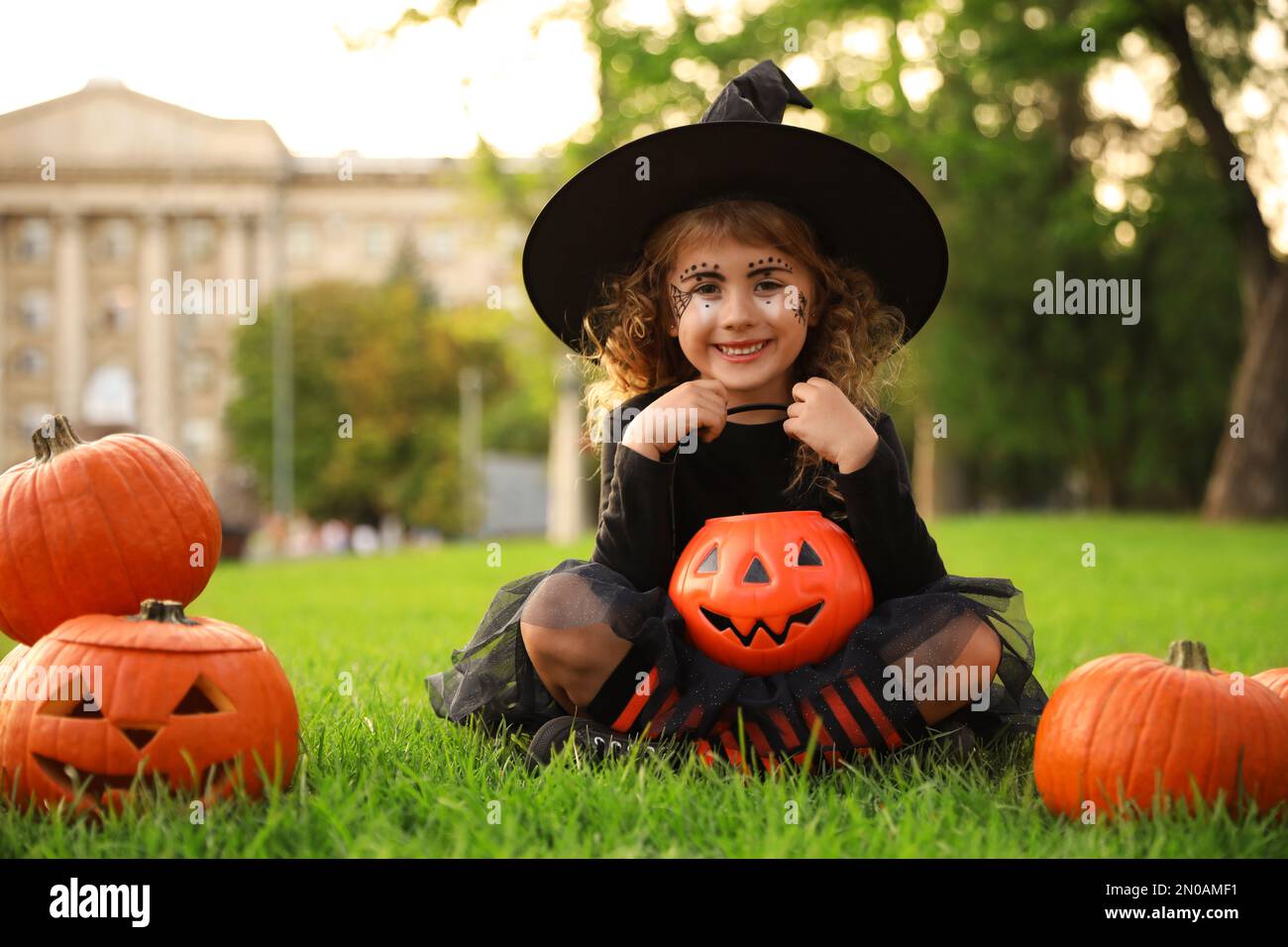 Petite fille mignonne avec un seau à bonbons de citrouille portant un costume d'Halloween dans le parc Banque D'Images