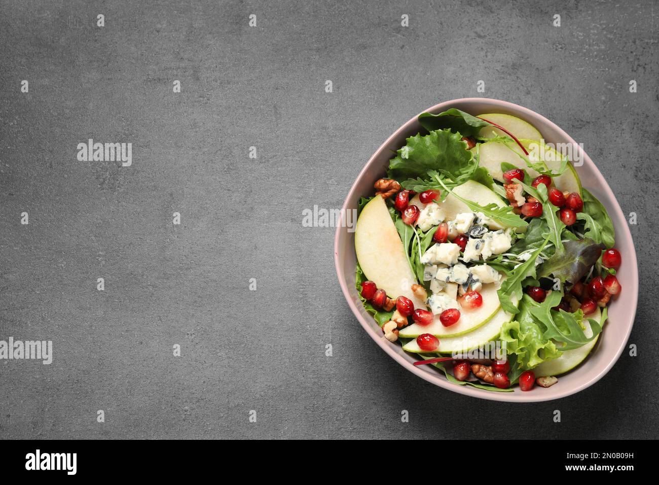 Salade savoureuse avec tranches de poire et graines de grenade sur table grise, vue du dessus. Espace pour le texte Banque D'Images