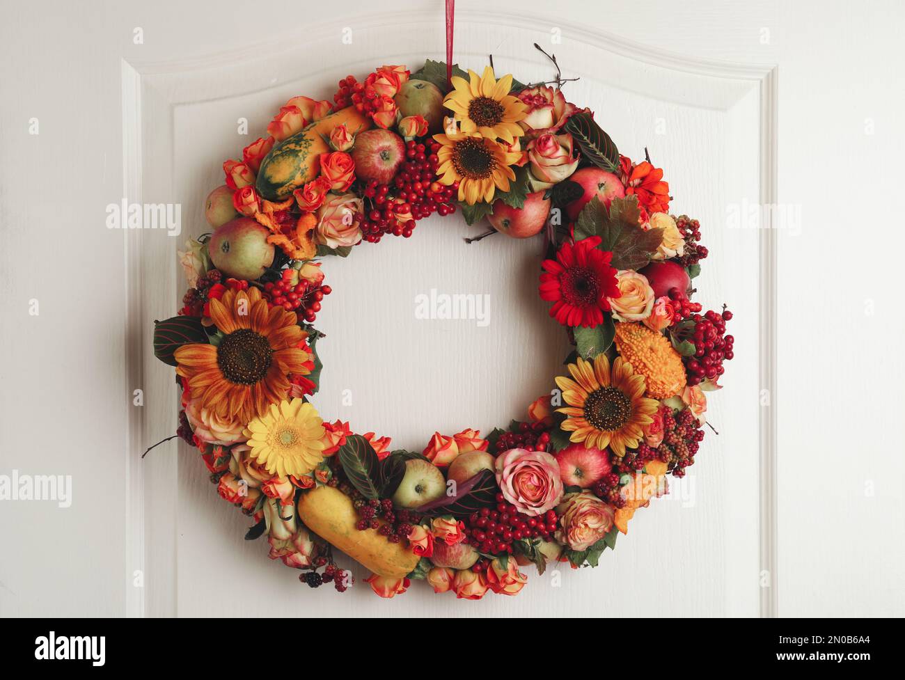 Belle couronne automnale avec fleurs, baies et fruits accrochés sur une porte en bois blanche. Espace pour le texte Banque D'Images