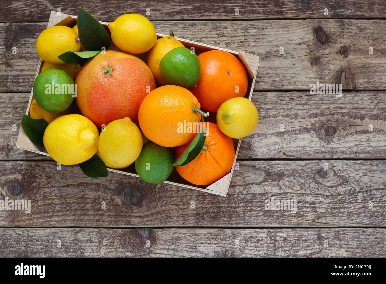 Mélange d'agrumes, d'oranges, de pamplemousses, de citrons et de limes avec feuilles dans une boîte sur fond de bois, vue du dessus. Photo ci-dessus. Banque D'Images