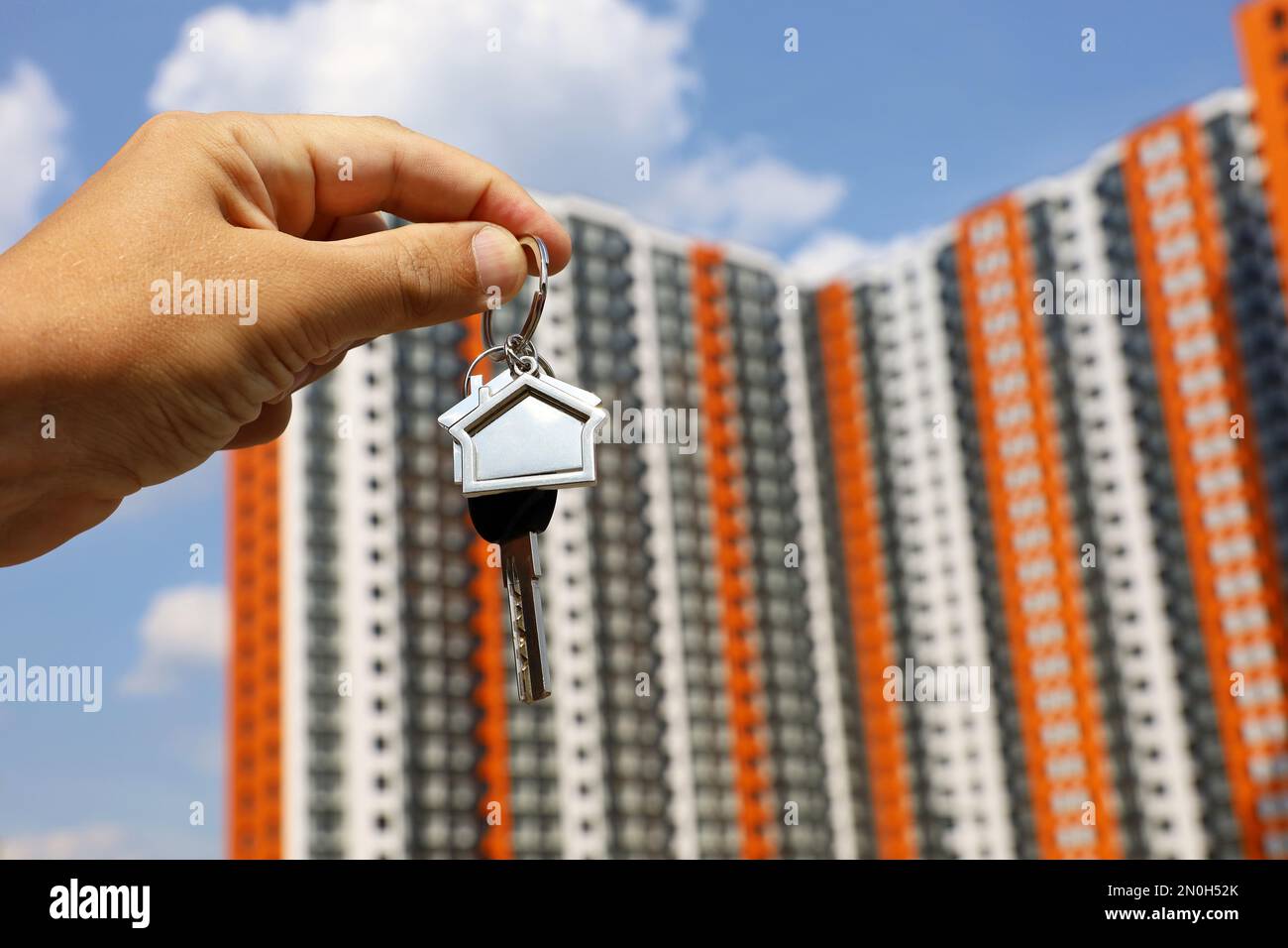 Clés de maison dans la main masculine sur fond de nouveaux bâtiments résidentiels. Agent immobilier, déménagement ou location de biens Banque D'Images