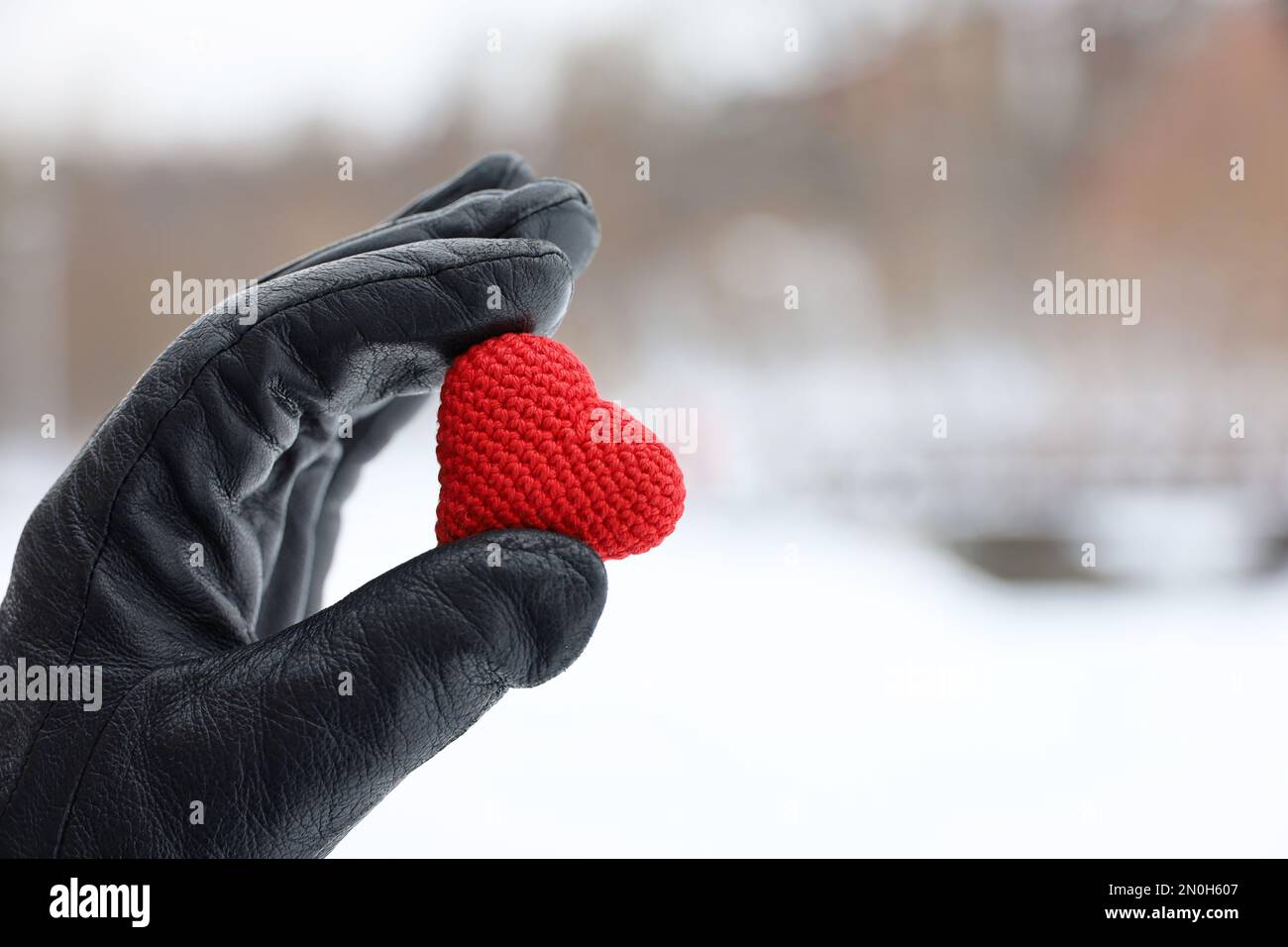 Coeur tricoté rouge dans la main femelle en cuir noir gant sur fond de parc à neige. Concept d'amour romantique, Saint-Valentin, temps d'hiver Banque D'Images