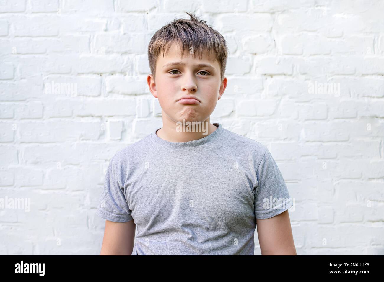 L'adolescent malheureux se tient à pouder près du mur de brique. Banque D'Images