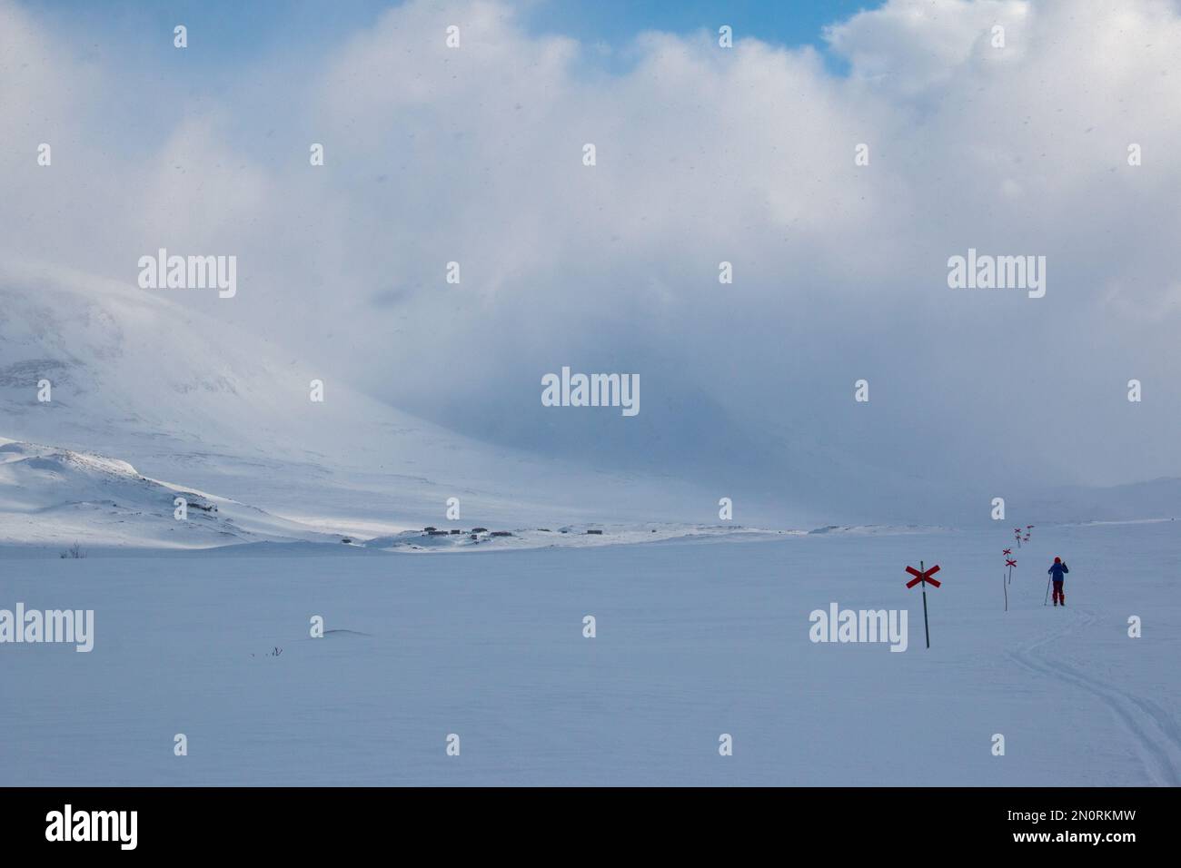 Un skieur sur le chemin des refuges de montagne d'Alesjaure (vus à distance) sur la piste de ski de Kungsleden en avril, Laponie, Suède Banque D'Images