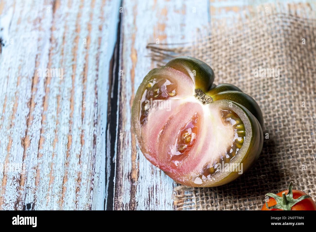 Image d'une tomate marmande mûre et douce en deux sur une toile de jute au-dessus d'une table bleue Banque D'Images
