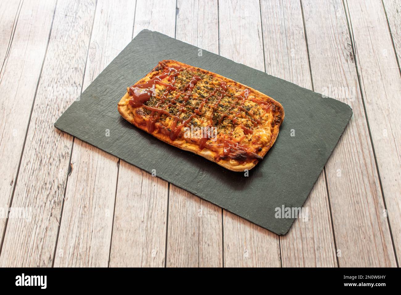 Une petite pizza barbecue rectangulaire sur un plateau en ardoise noire Banque D'Images
