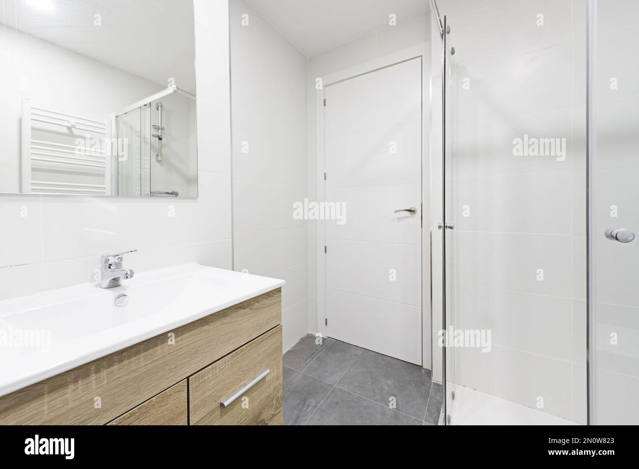 salle de bains avec lavabo en bois sous un miroir mural sans cadre, douche à l'italienne avec cloisons et portes en bois blanc Banque D'Images