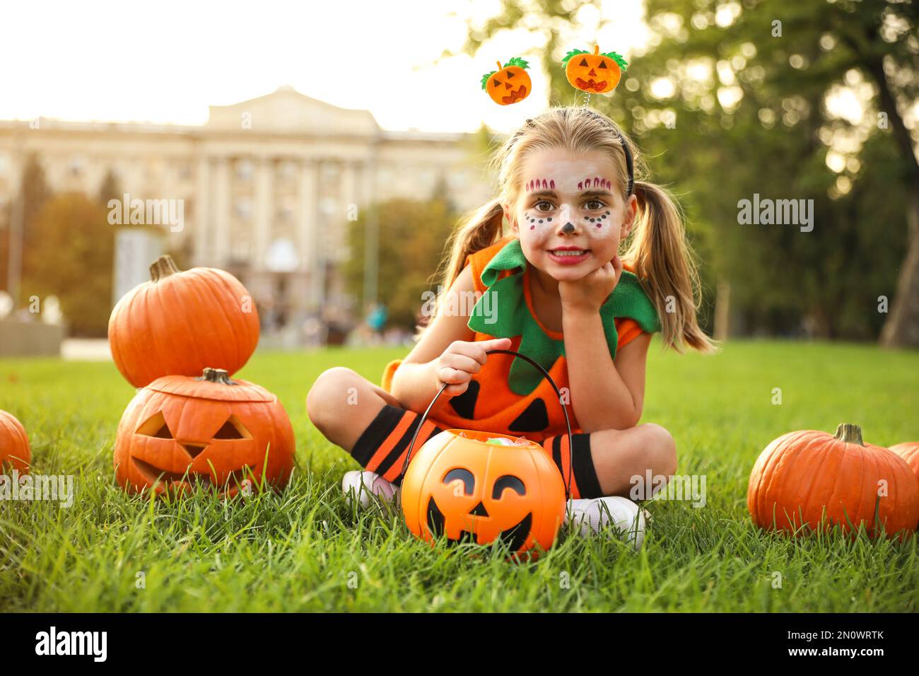 Petite fille mignonne avec un seau à bonbons de citrouille portant un costume d'Halloween dans le parc Banque D'Images