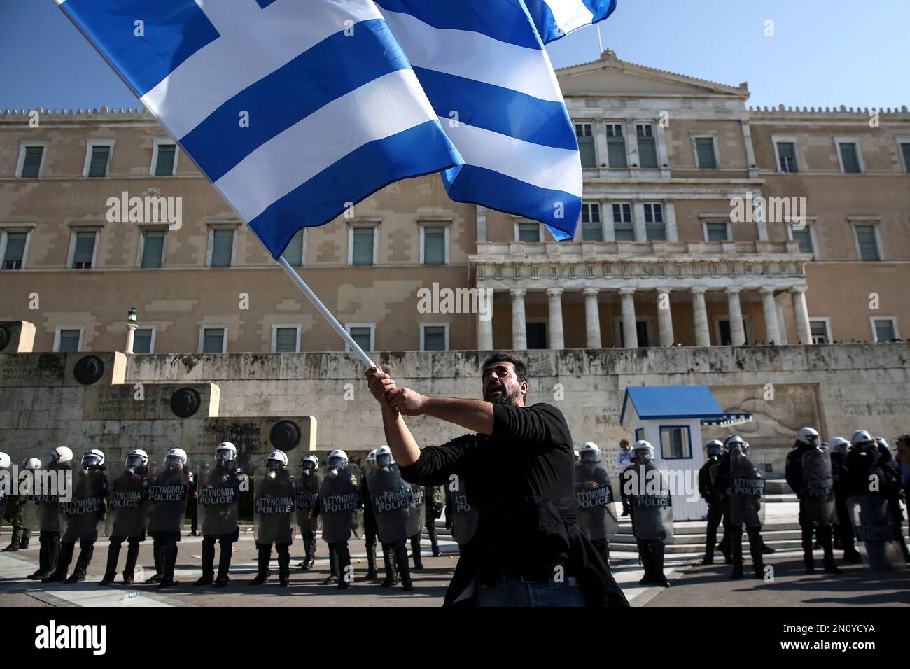 A farmer waves a Greek flag in front of riot policemen standing guard in front of the parliament during an anti-government protest at central Syntagma square in Athens, Wednesday, Nov. 18, 2015. Greek farmers protesting over planned tax and pension reforms demanded by the country's bailout creditors have clashed outside parliament with police, who used tear gas to disperse them. (AP Photo/Yorgos Karahalis) Banque D'Images