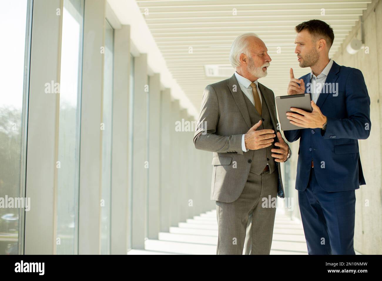 Un jeune homme d'affaires et un homme d'affaires senior descendent dans le couloir d'un bureau, profondément dans la conversation. Ils sont tous deux habillés professionnellement, reflétant leur acum d'affaires Banque D'Images