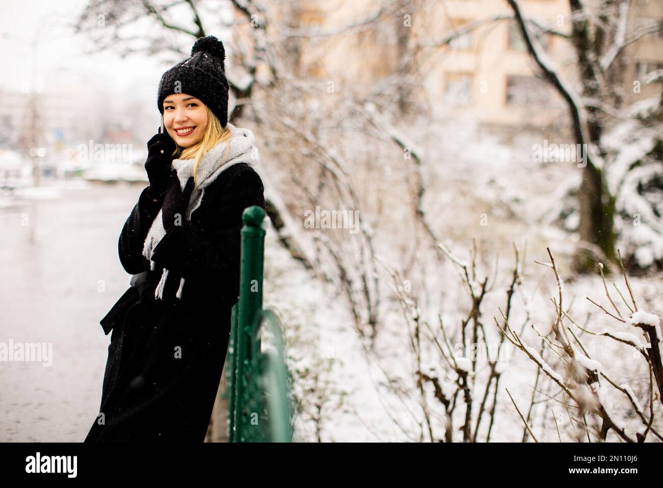 Jolie jeune femme dans des vêtements chauds utilisant un téléphone portable lors d'une journée d'hiver Banque D'Images