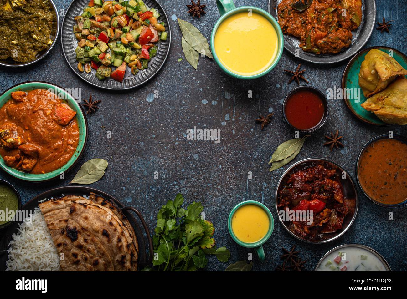 Buffet de nourriture ethnique indienne sur table en béton d'en haut: Curry, samosa, riz biryani, dal, paneer, chapatti, naan, tikka masala de poulet, lassi de mangue, d Banque D'Images