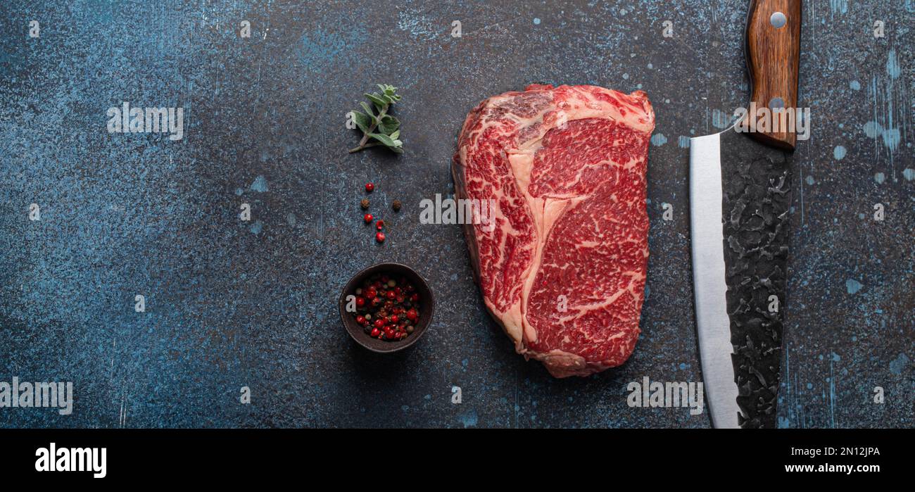Bœuf à la viande cru bœuf marbré steak de première qualité Ribeye sur fond rustique de table de cuisine en béton d'en haut avec un grand couteau et des épices, beefsteak concept espace Banque D'Images