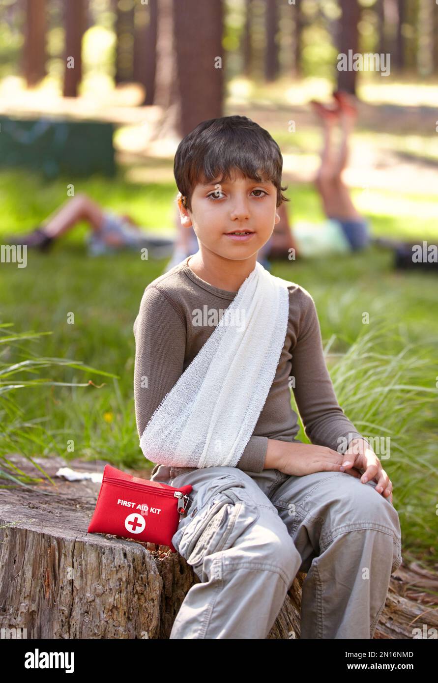 Pourquoi ai-je dû me faire mal. Un jeune garçon avec son bras dans une élingue assise sur une souche d'arbre. Banque D'Images