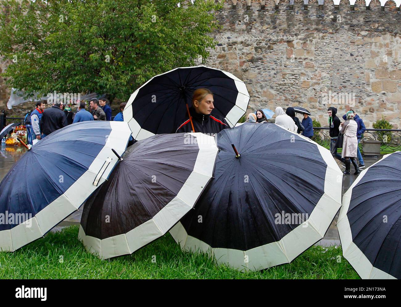 A woman stands with umbrellas as people gather at Svetitskhoveli Cathedral to attend celebrations of a religious holiday in the Georgian ancient capital Mtskheta outside Tbilisi, Georgia, Wednesday, Oct. 14, 2015. Svetitskhoveli Cathedral, known as the burial site of Christ's mantle, is the principal Georgian church and one of the most venerated places of worship. (AP Photo/Shakh Aivazov) Banque D'Images
