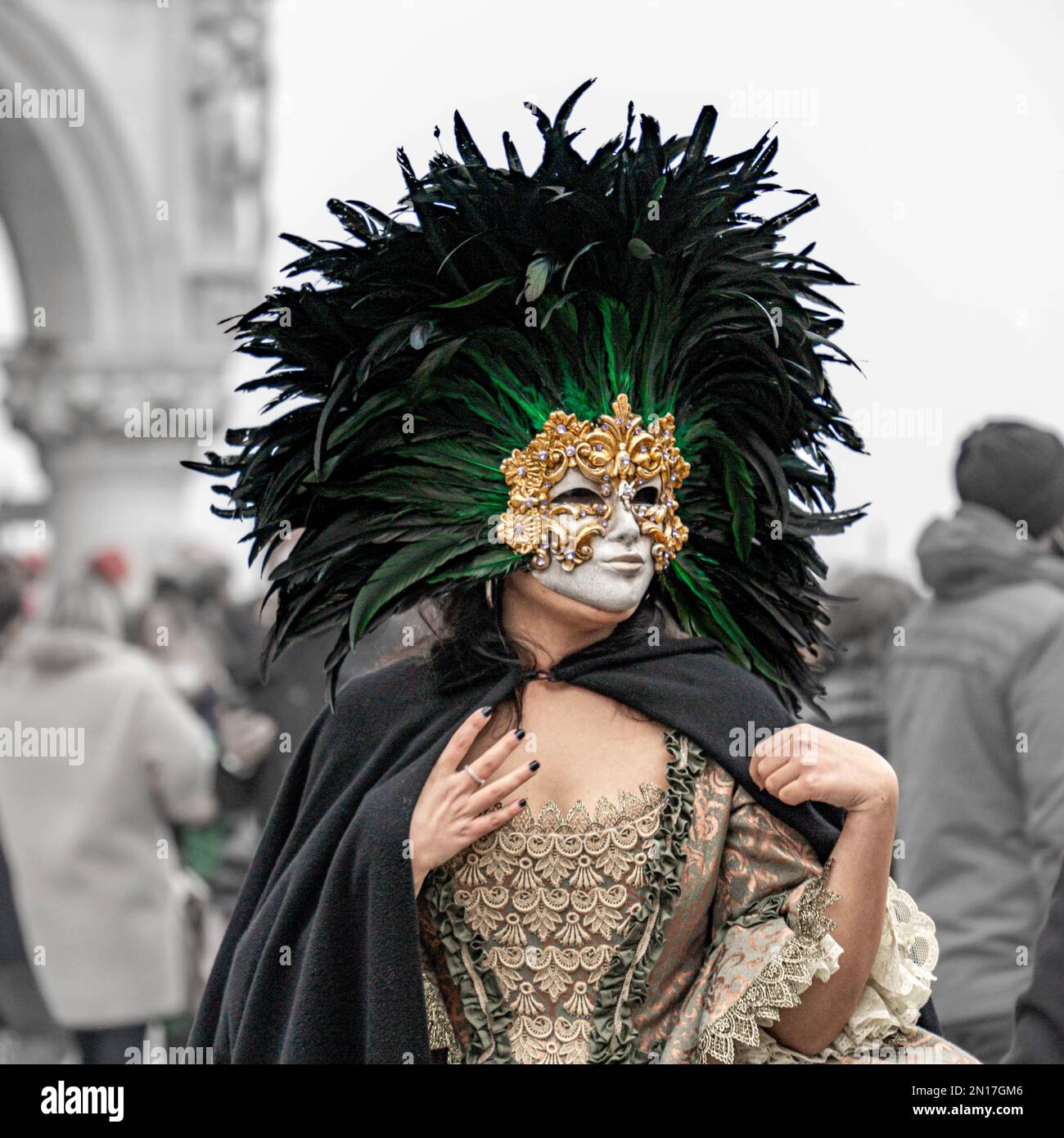 Carnaval de la Vinèce. Une femme en costume vintage avec une dentelle, portant un masque de carnaval doré bordé d'un cercle de plumes noires élevées, se tient seule Banque D'Images