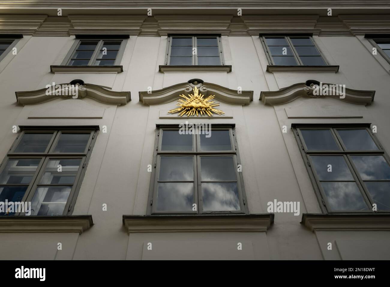 Élément de décor doré du troisième œil entouré de nuages et d'éléments de foudre sur une grande fenêtre reflétant les nuages d'un vieux bâtiment haut à Vienne, Banque D'Images