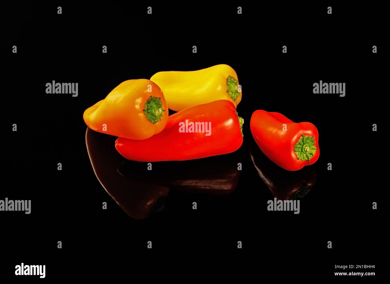 Le paprika multicolore se reflète dans une table miroir noire. Banque D'Images