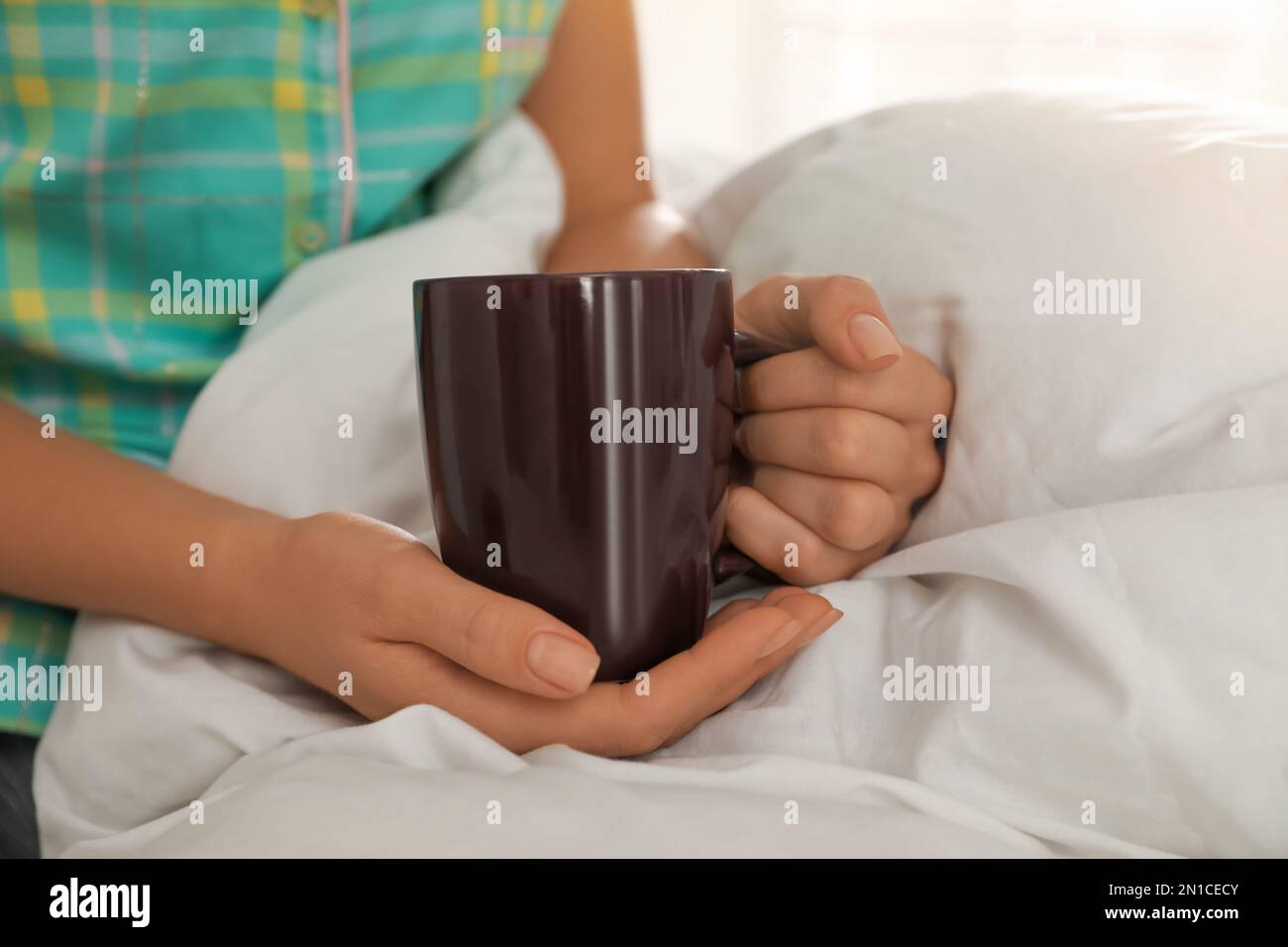 Femme avec une tasse au lit à la maison, en gros plan Banque D'Images