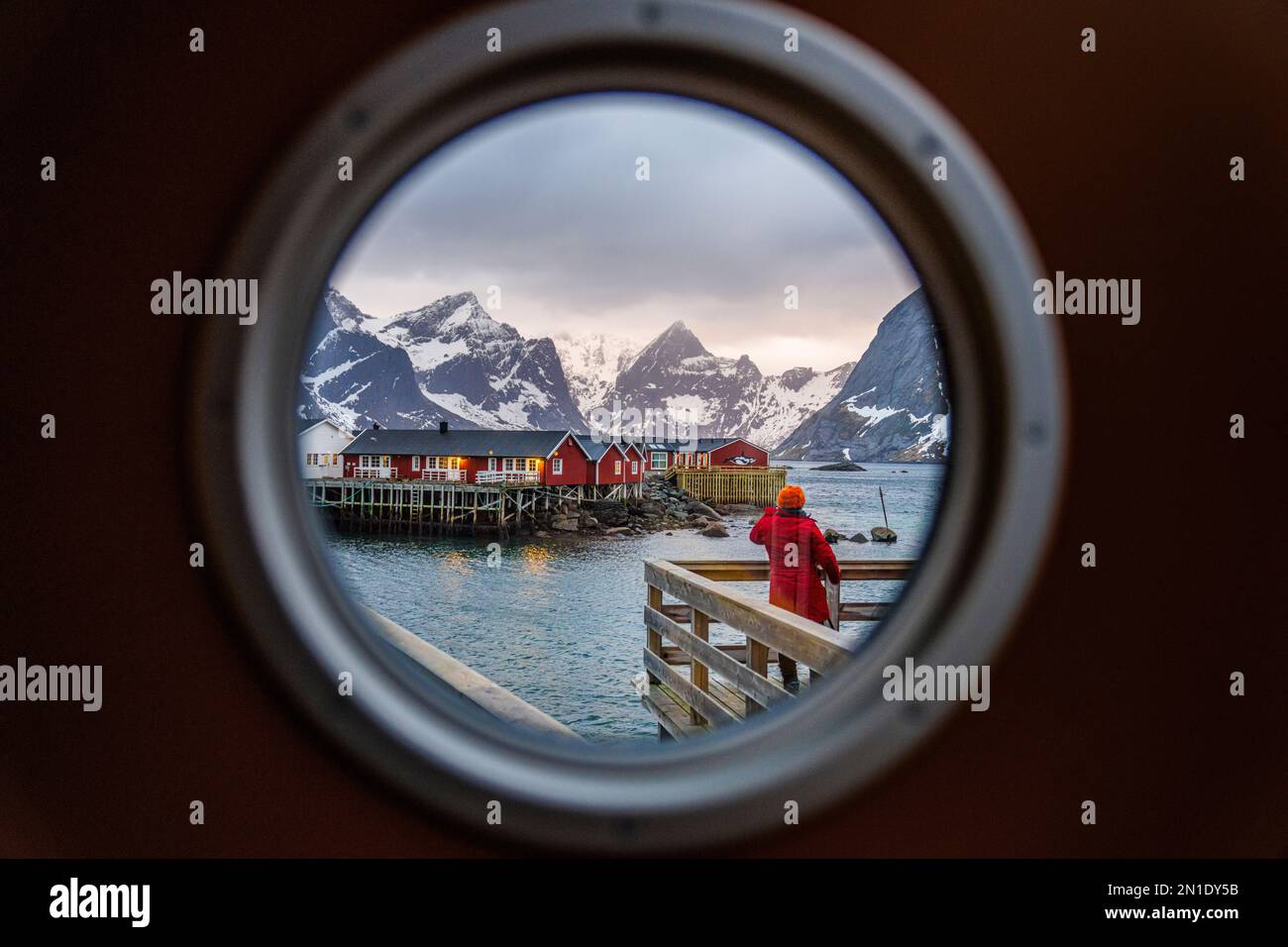 Vue arrière de la personne regardant les cabines traditionnelles de rorbu vue à travers un hublot, Reine Bay, îles Lofoten, Norvège, Scandinavie, Europe Banque D'Images