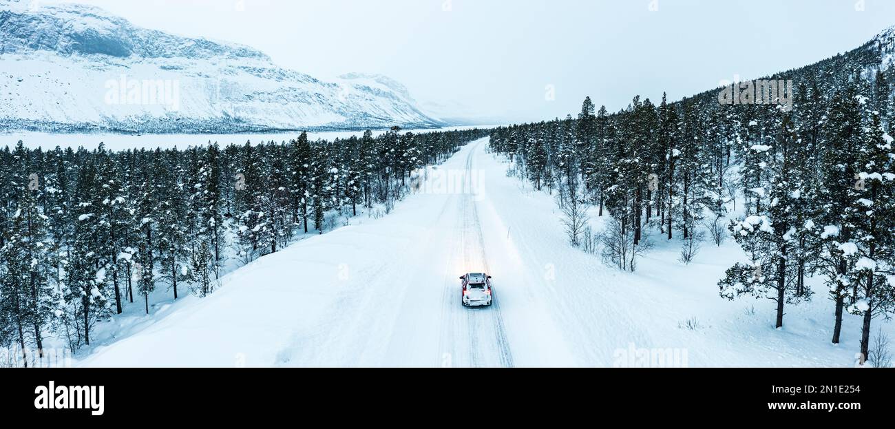 Vue aérienne de la voiture conduite sur une route glacée traversant une forêt couverte de neige, Stora Sjofallet, Comté de Norrbotten, Laponie, Suède, Scandinavie, Europe Banque D'Images