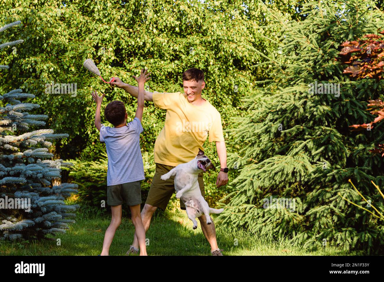 Un père et un fils qui rient en jouant à l'extérieur avec un chien de compagnie de famille Banque D'Images