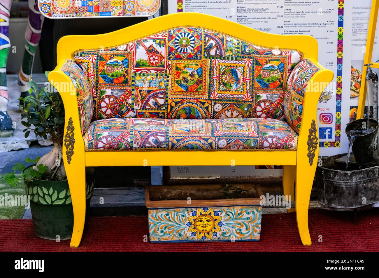 Taormina Sicile Italie, banc jaune vif avec patchwork coloré revêtements devant un restaurant dans la vieille ville de Taormina Banque D'Images