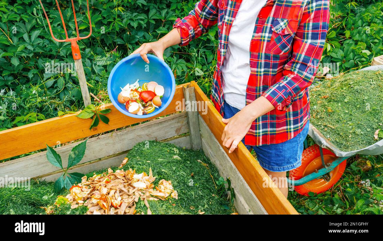 Déchets de cuisine, coupures de pelouse comme ingrédients de compostage gros plan. Une femme jette les déchets alimentaires dans un bac de compost en bois. Maintien de l'agriculture biologique Banque D'Images