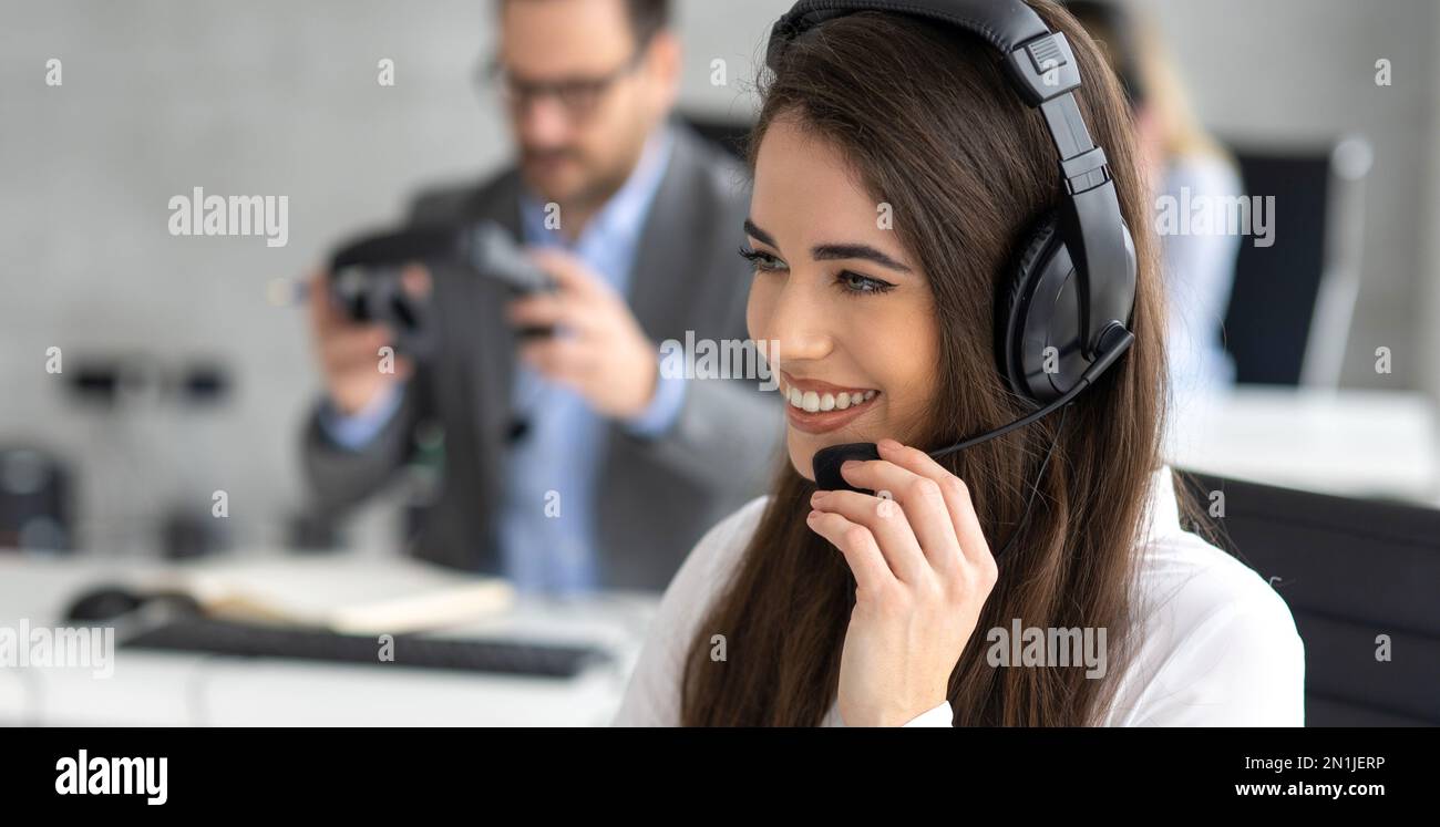 Photo d'une belle jeune femme travaillant dans un centre d'appels. Un agent amical du centre d'appels tient le microphone tout en parlant avec le client. Banque D'Images