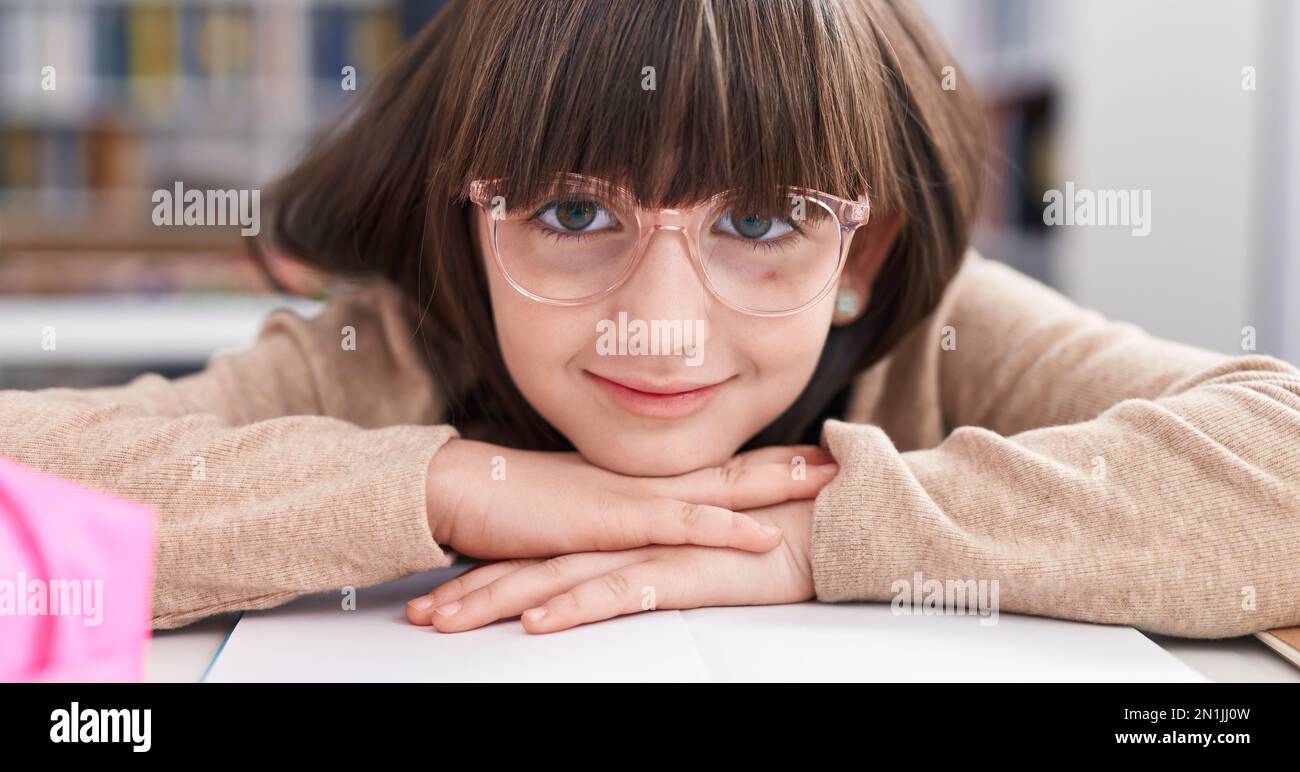 Adorable étudiante hispanique de fille assise sur une table penchée sur le livre en classe Banque D'Images