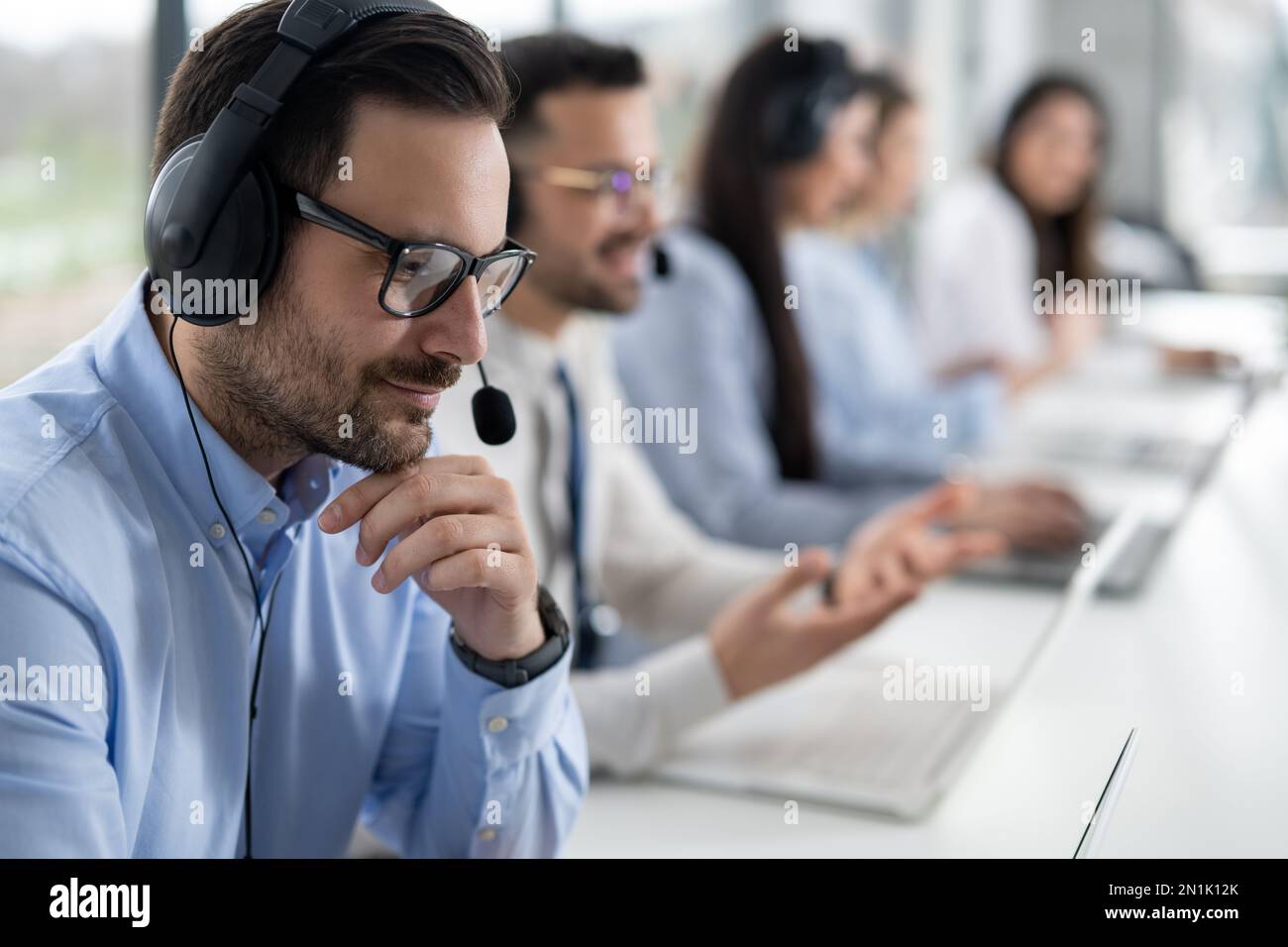 Gros plan sur un agent d'assistance clientèle de sexe masculin, avec un micro-casque travaillant dans le centre d'appels. Groupe d'opérateurs d'assistance au service de prise en charge des clients Banque D'Images