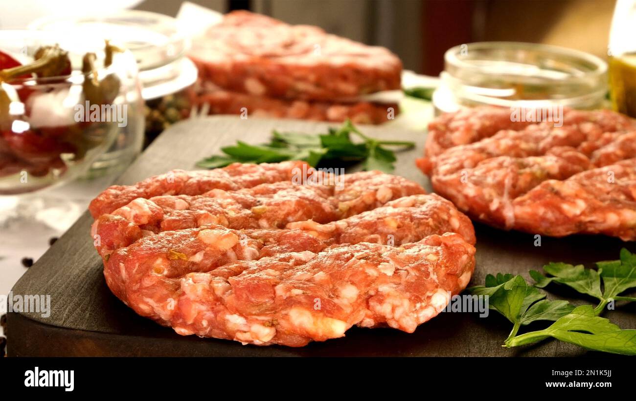 Arrondir la côtelette de hamburger de bœuf haché cru frais avec des épices et de la sauce sur un plan de cuisine sombre. Ingrédient pour la préparation de hamburgers dans la cuisine. Haut vi Banque D'Images