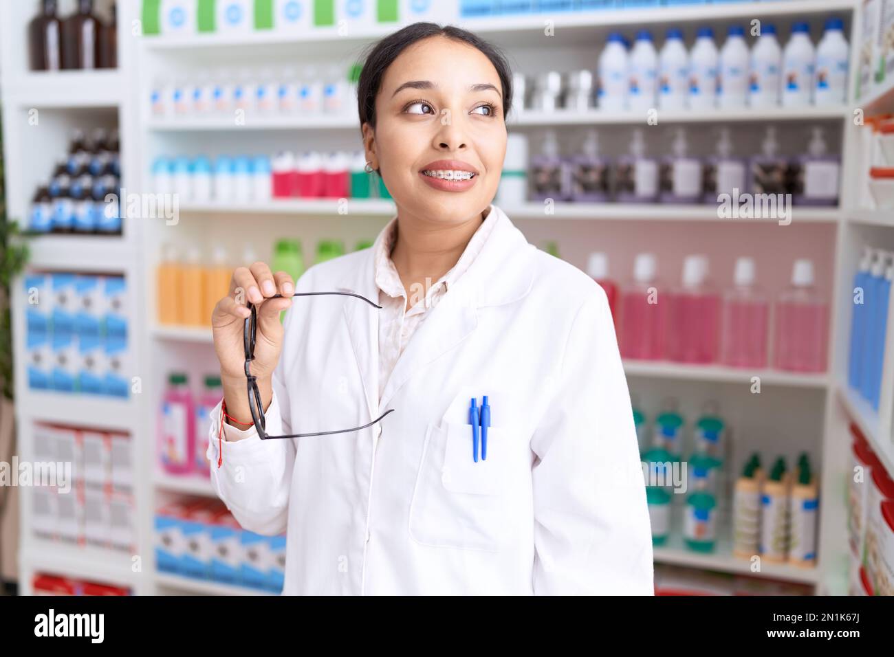 Jeune femme arabe pharmacien souriant confiant tenant des lunettes à la pharmacie Banque D'Images