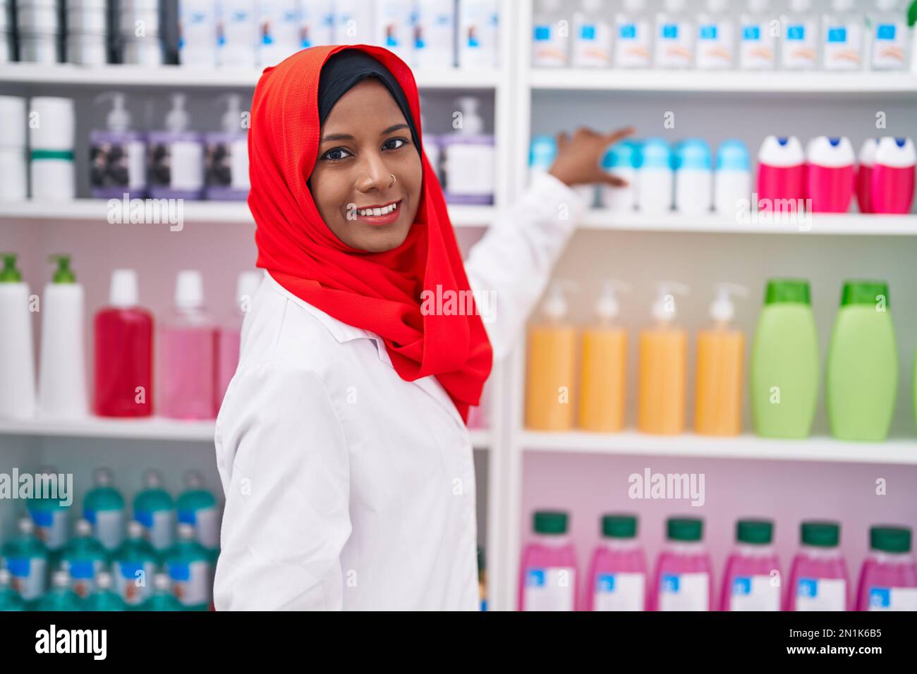Jeune belle femme pharmacien souriant confiant tenant des médicaments sur des étagères à la pharmacie Banque D'Images