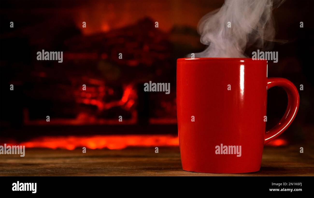 Une tasse de boisson chaude à la vapeur, du café ou du thé sur une planche à bois, près d'une cheminée. La vapeur s'échappe de la tasse. Copier l'espace. Gros plan. Banque D'Images