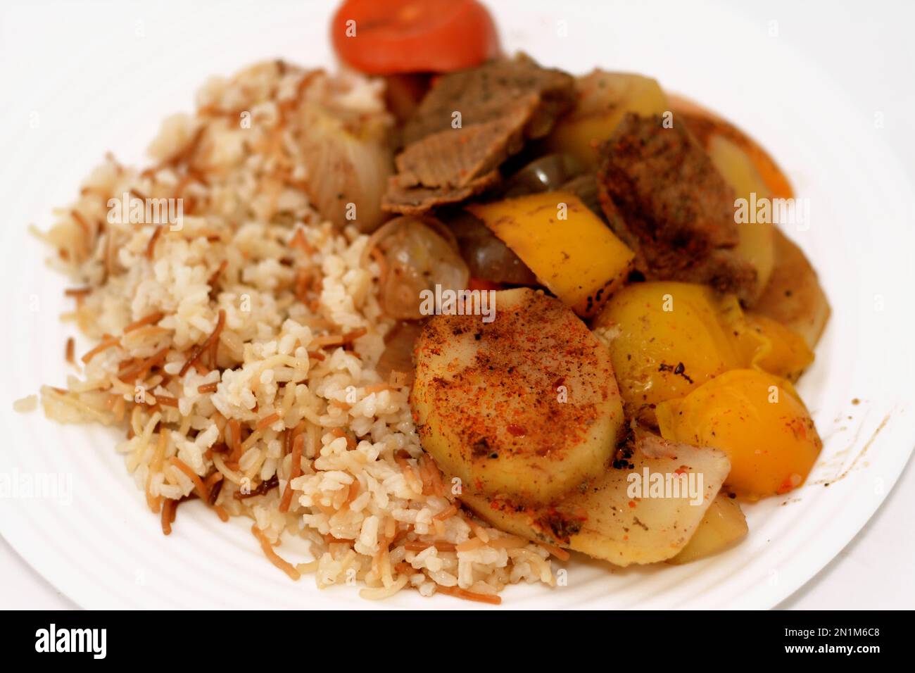 Une assiette de riz égyptien avec vermicelles cuites à la vapeur chaude avec des tranches de pommes de terre cuites au four, oignon, tomate, poivre coloré, morceaux de viande, épices, guar Banque D'Images