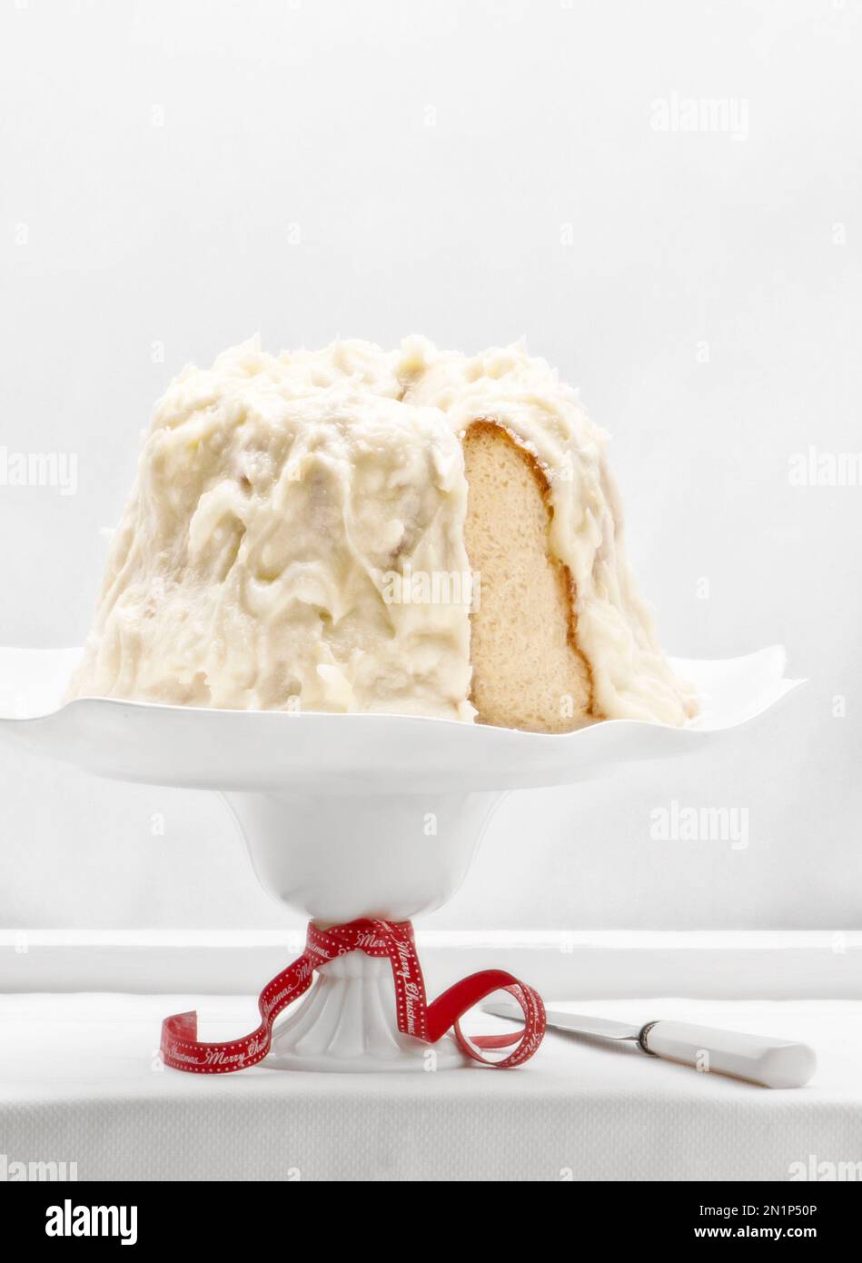 Gâteau Angel Food avec glaçage au citron. Fond blanc total , assiette blanche , couteau et un ruban rouge de Noël, Joyeux Noël. Cuisine de saison Banque D'Images