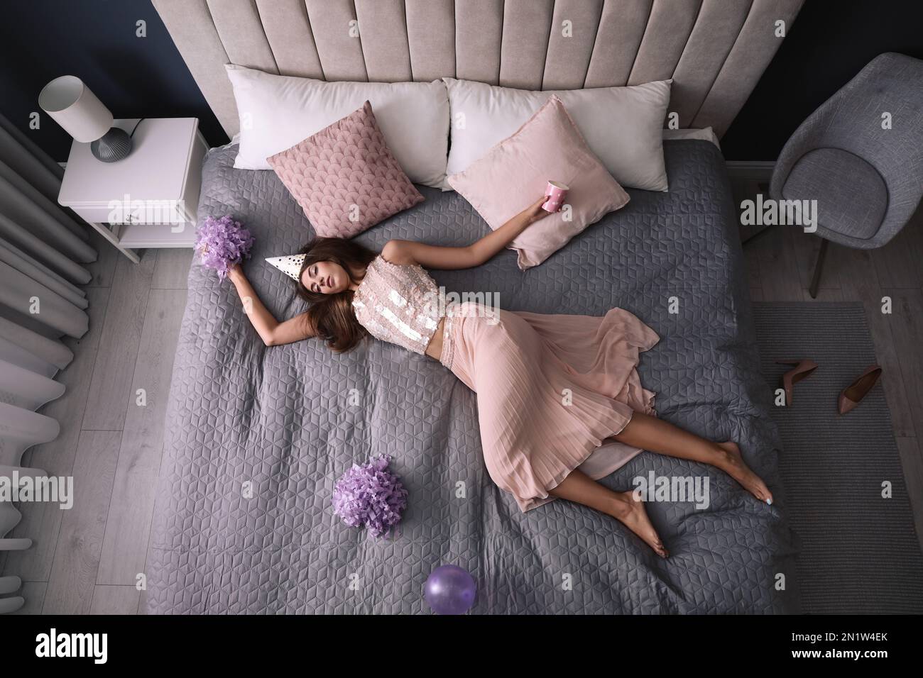 Femme épuisée en tenue de fête dormant sur le lit à la maison après la fête, au-dessus de la vue Banque D'Images