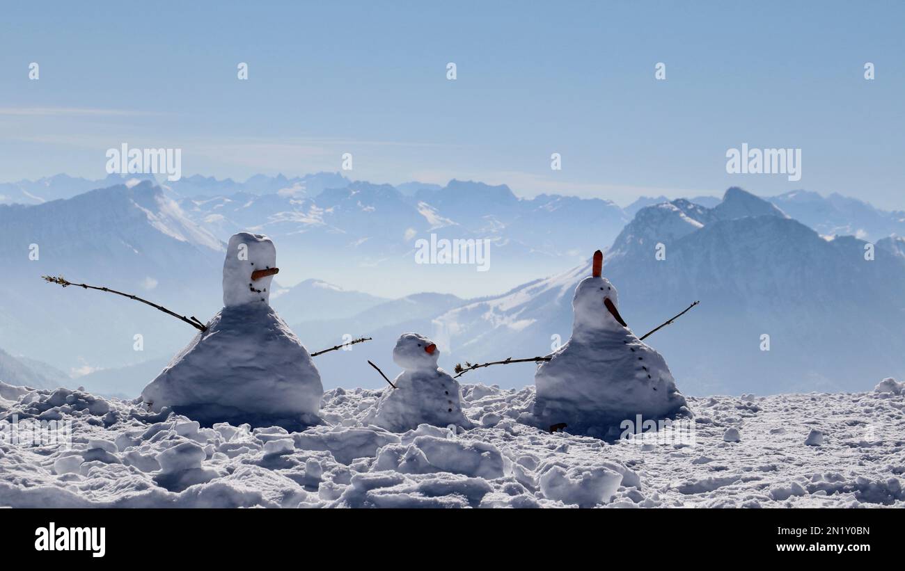 Trois tailles différentes d'hommes de neige sur un terrain enneigé avec des montagnes en arrière-plan par une journée d'hiver ensoleillée Banque D'Images