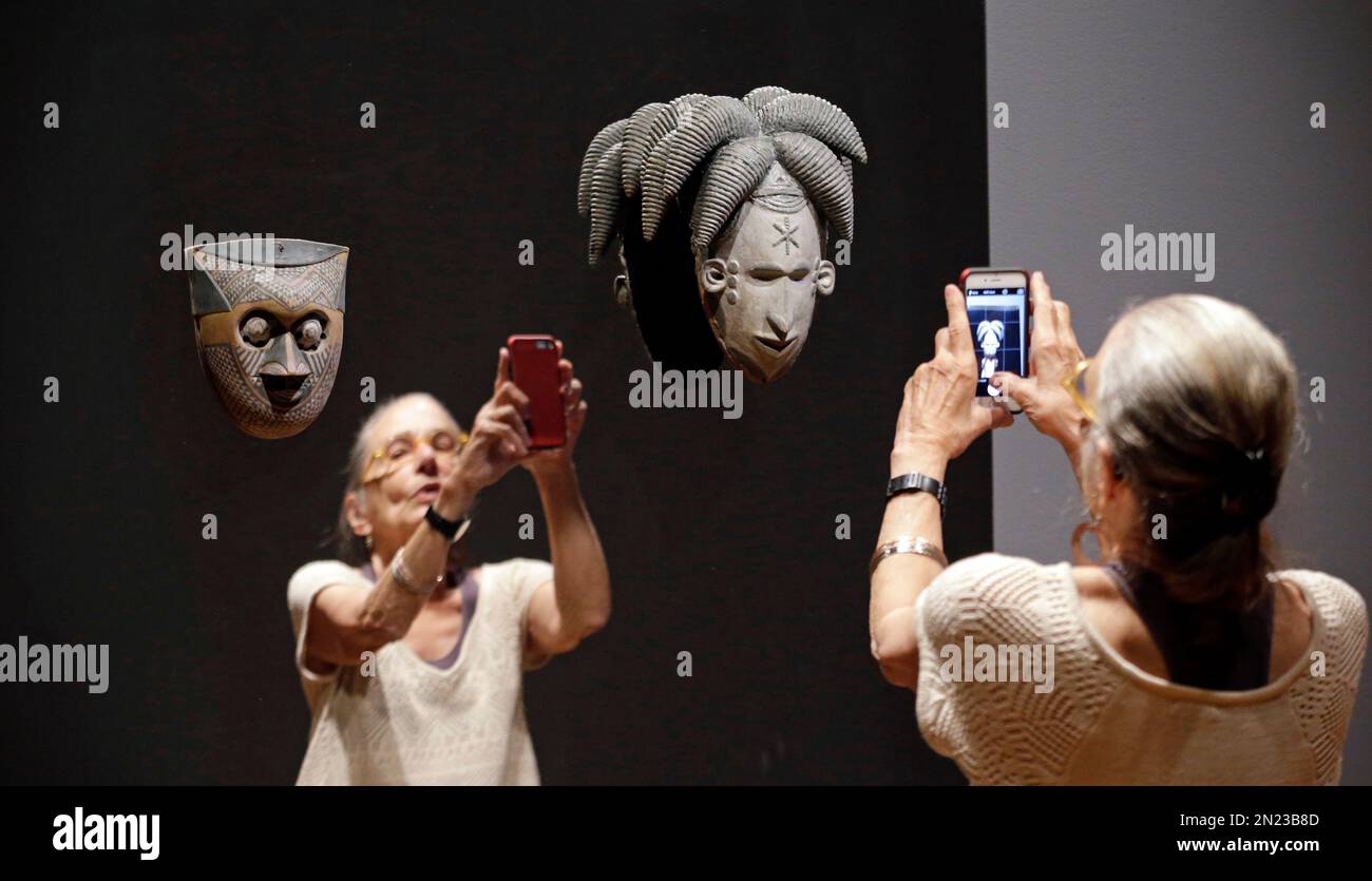 Kara Jakobs tries to take a photo of herself with a mask mounted on a mirror as part of the the show “Disguise: Masks & Global African Art” at the Seattle Art Museum on Sunday, June 28, 2015, in Seattle. Race, identity and the masks people wear are the themes explored in the new exhibit of contemporary, multimedia art, which showcases masks from the museum’s collection alongside contemporary art, much of it created just for this show by African artists and those of African descent. The show will be traveling to Los Angeles and New York after Seattle. (AP Photo/Elaine Thompson) Banque D'Images