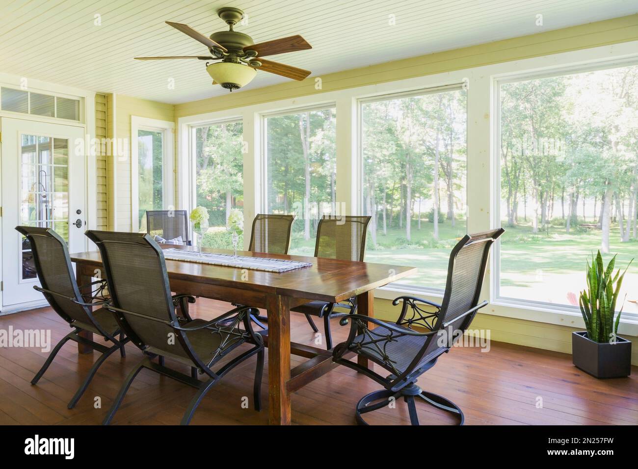 Table à manger en bois antique et chaises à dossier haut dans la salle de soleil avec plancher de planche de cèdre teinté à l'intérieur de la maison de style cottage contemporain. Banque D'Images