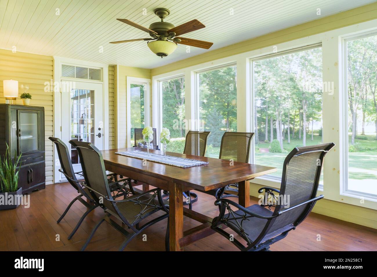 Table à manger en bois antique et chaises à dossier haut dans la salle de soleil avec plancher de planche de cèdre teinté à l'intérieur de la maison de style cottage contemporain. Banque D'Images