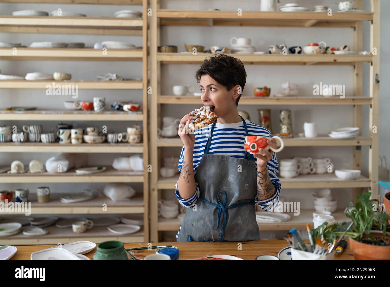 Une femme détendue à l'aide d'un tablier boit du café dans une tasse en  céramique artisanale et a un en-cas dans un studio de poterie Photo Stock -  Alamy