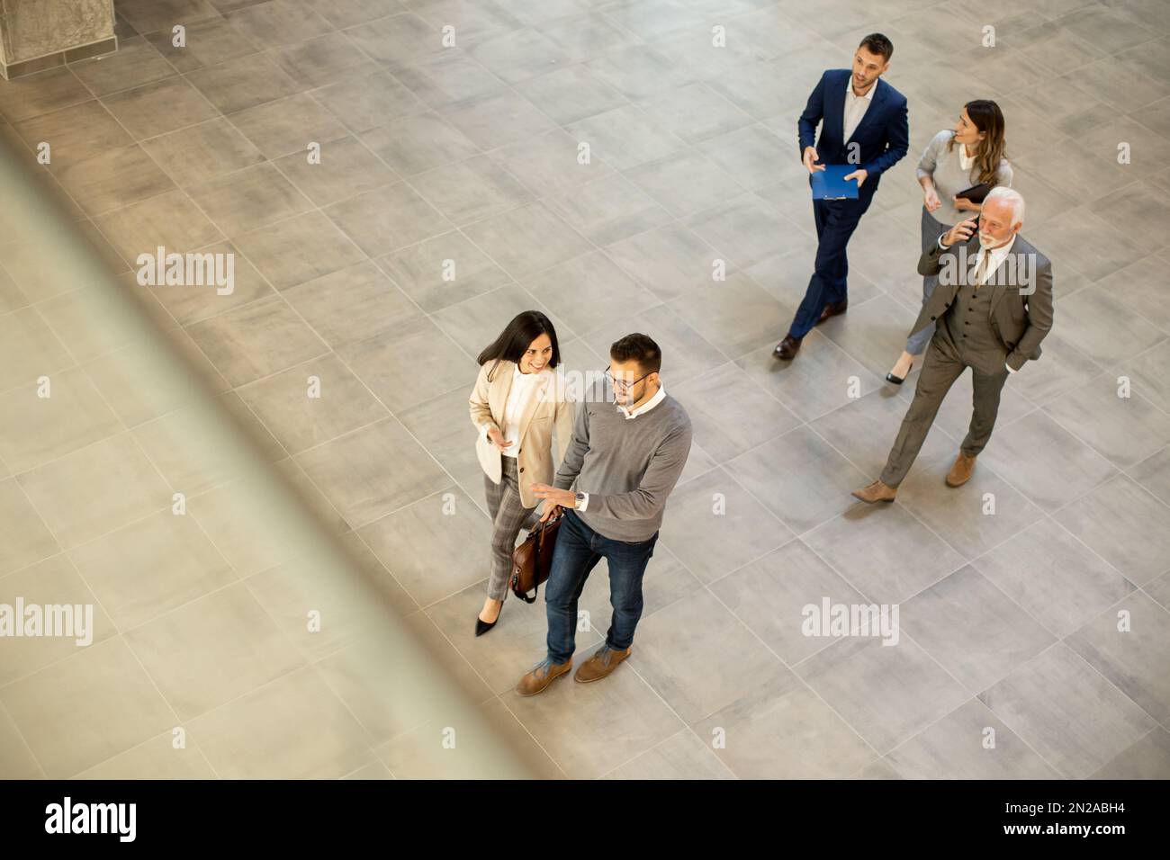 Un groupe de jeunes et de personnes âgées en voyage d'affaires se prompe dans un couloir de bureau, capturé dans une vue aérienne. Ils sont vêtus d'une tenue habillée, ils marchent avec humour Banque D'Images